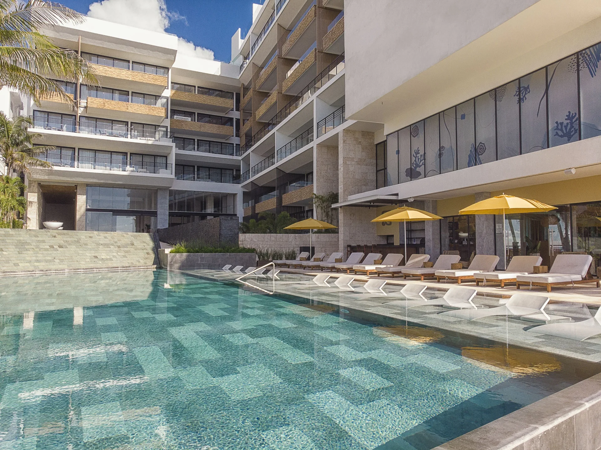 Pool with loungers and yellow umbrellas at The Fives Oceanfront Riviera Maya.