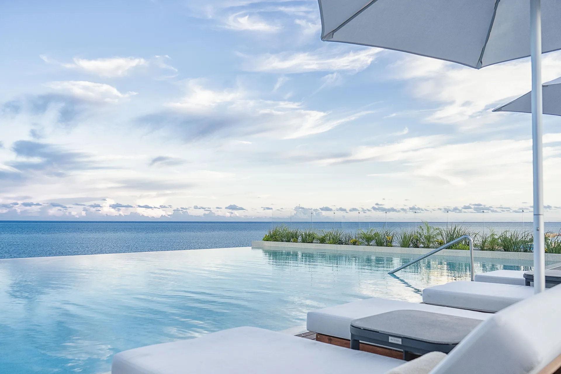 Rooftop infinity pool with ocean view and white umbrellas at The Fives Oceanfront Riviera Maya.