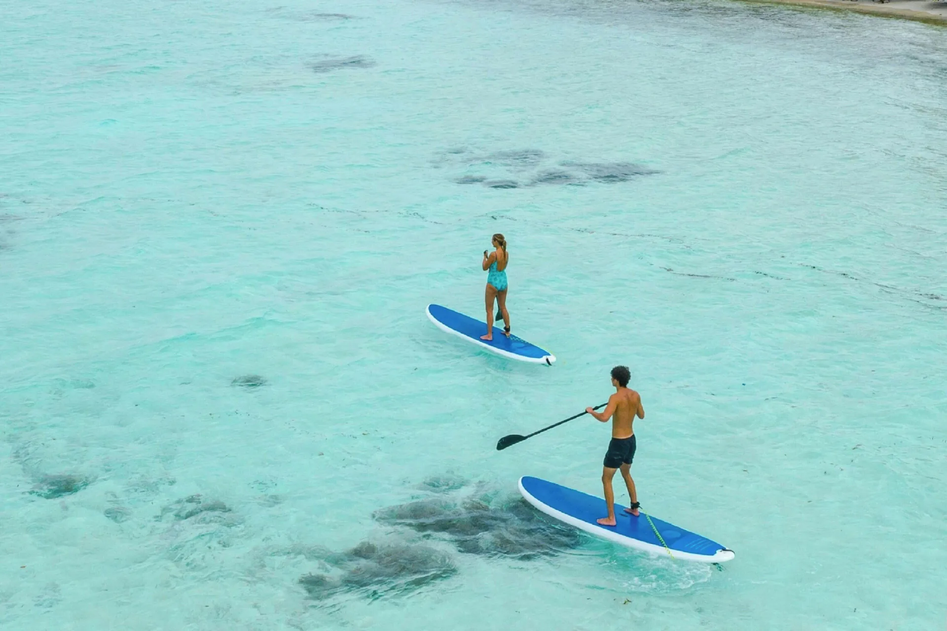 Two guests paddleboarding over clear turquoise water at The House.