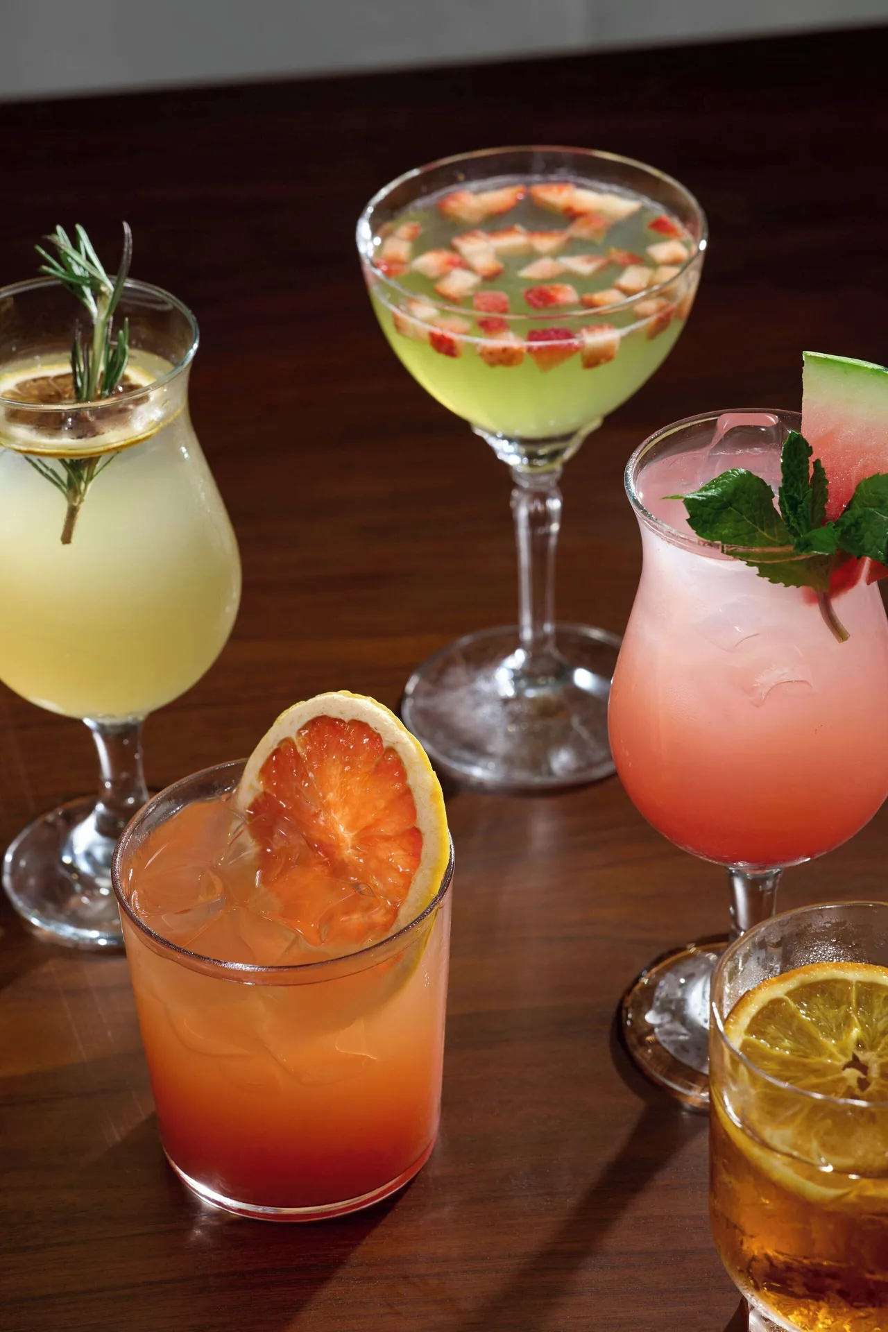 Colorful cocktails with fruit and herb garnishes on a wooden table at The House.