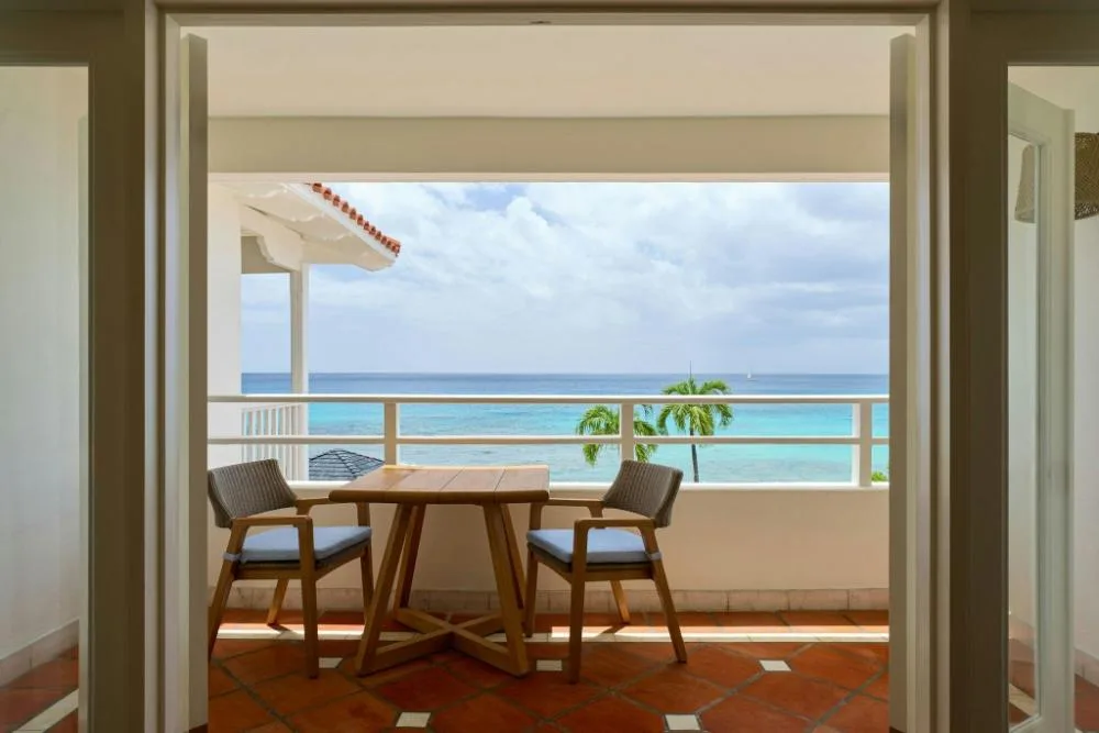 Balcony of an Ocean View 1 Bedroom Suite at The House with table, chairs, and sea beyond the railing.