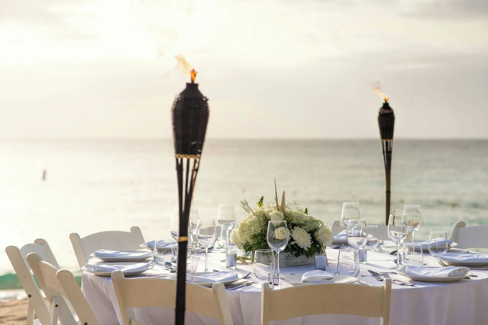Beachfront event table with white flowers and torches by the sea at The House.