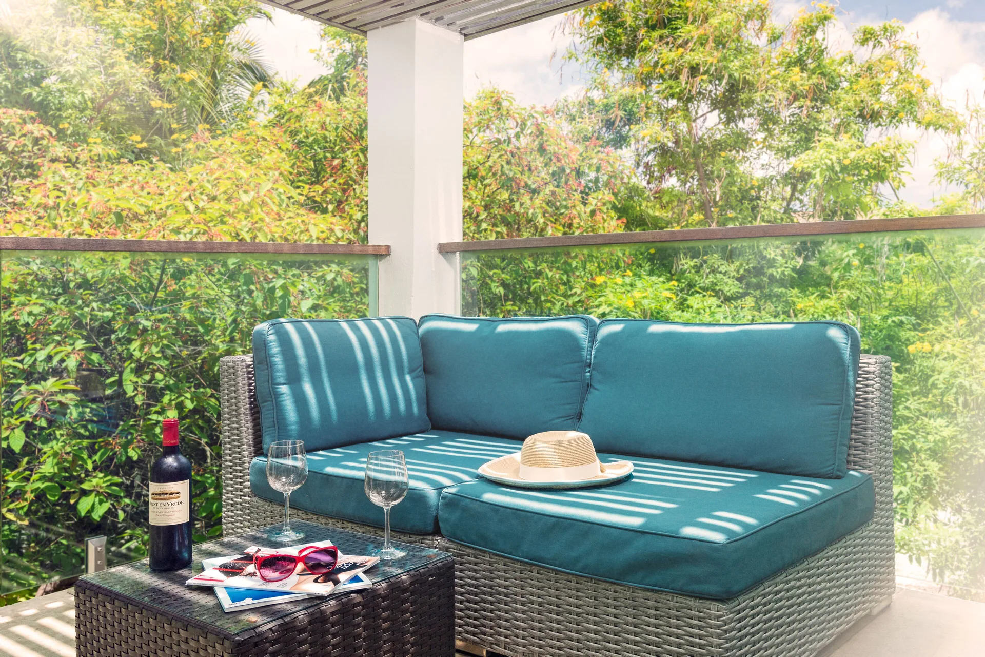 Luxury Room balcony sofa with glasses and leafy view at The Oasis at Grace Bay.