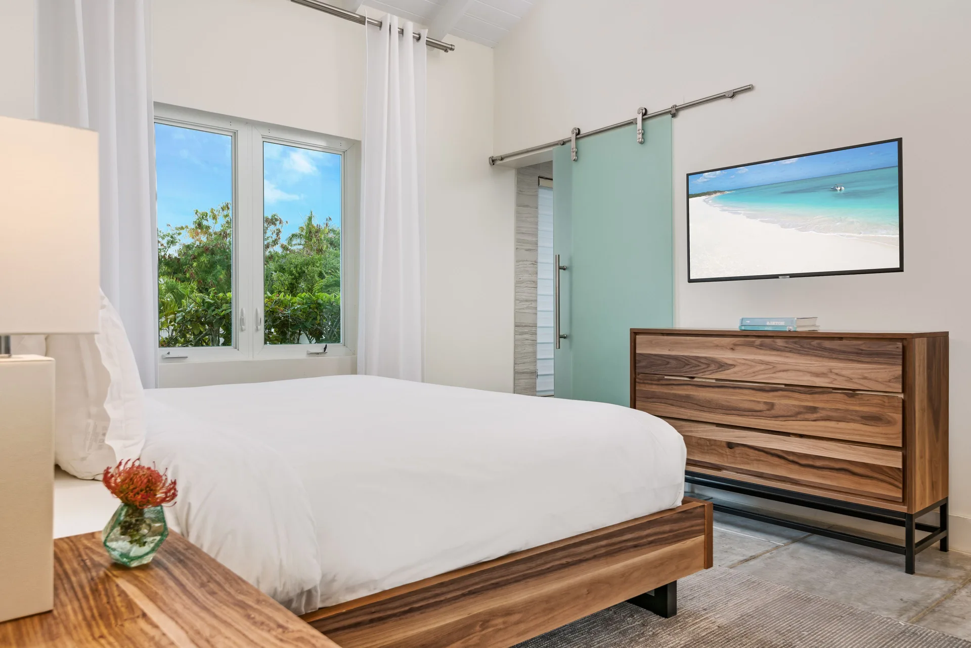 Luxury Villa bedroom with wood bed, dresser, TV and frosted sliding door at The Oasis at Grace Bay.