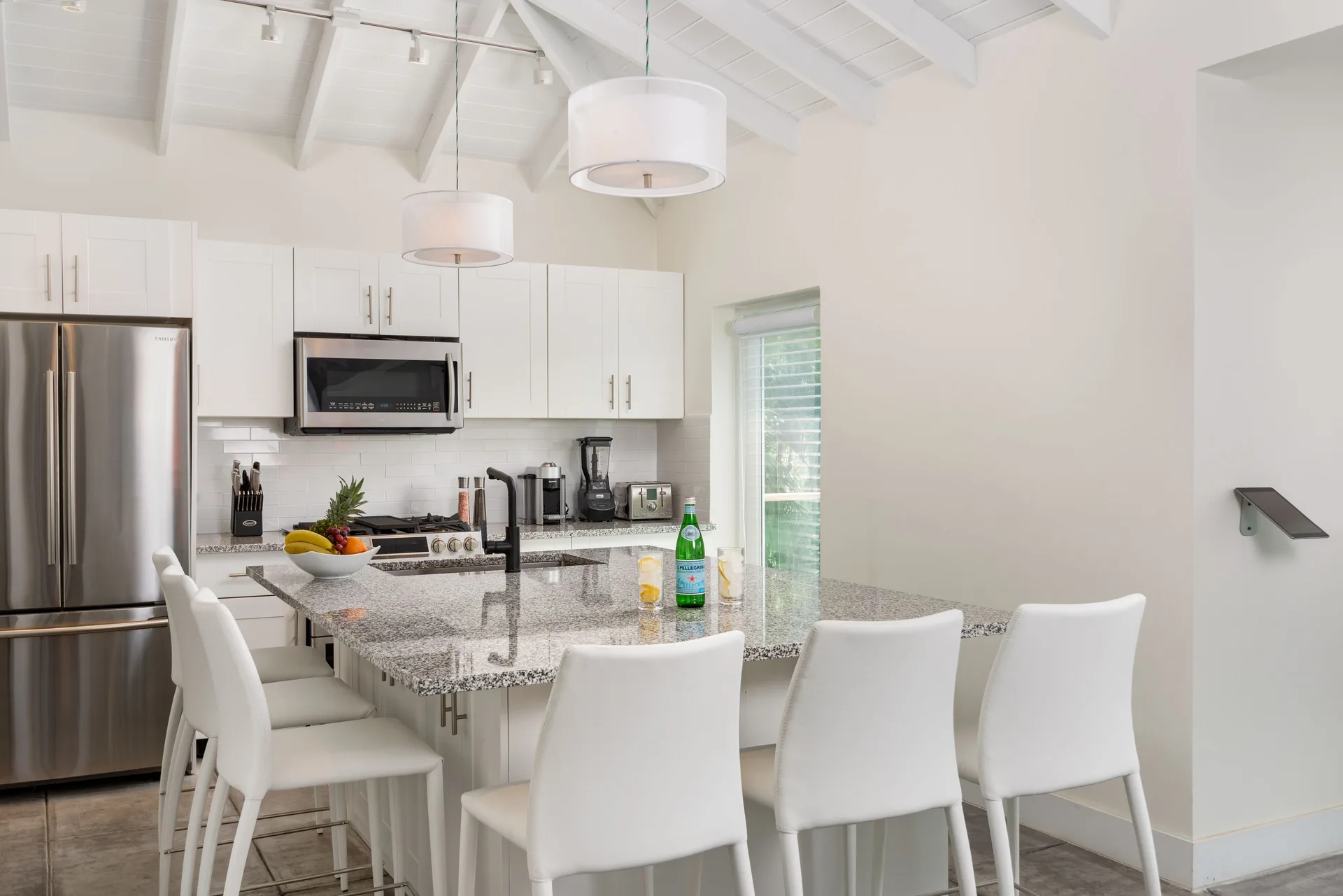 White villa kitchen with granite island, bar chairs, and stainless appliances at The Oasis at Grace Bay.