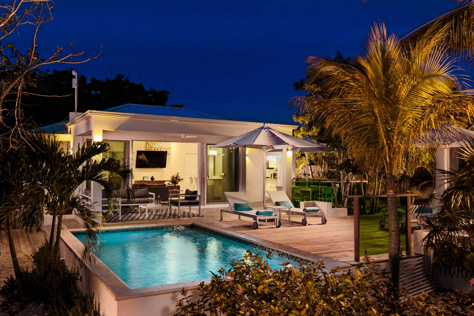 Luxury Villa pool terrace at night with illuminated water and palm trees at The Oasis at Grace Bay.