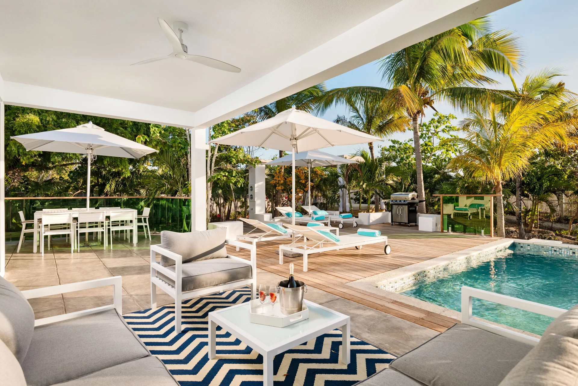 Covered villa patio with pool, loungers, dining table, and palm trees at The Oasis at Grace Bay.