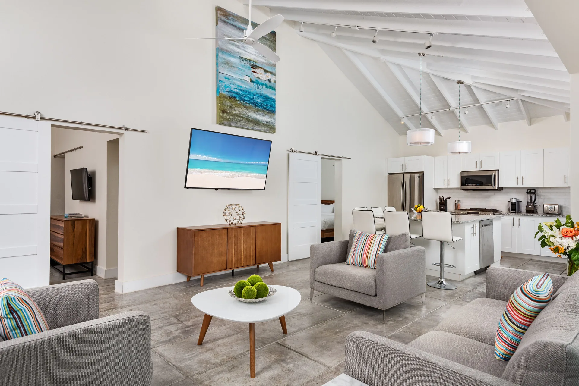Spacious villa living area with armchairs, TV, kitchen island, and vaulted ceiling at The Oasis at Grace Bay.
