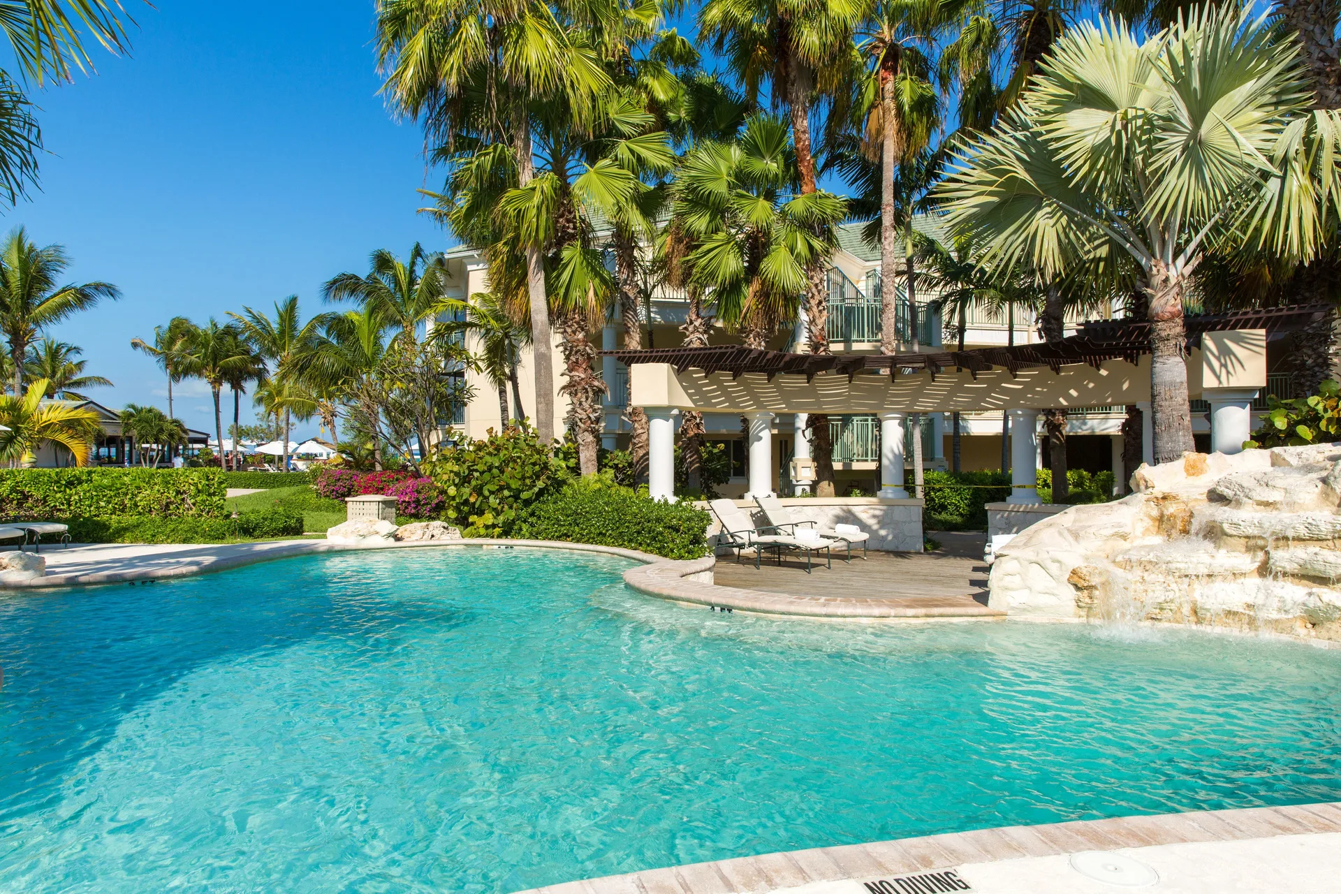 Curved resort pool with palms and a waterfall at The Sands at Grace Bay.