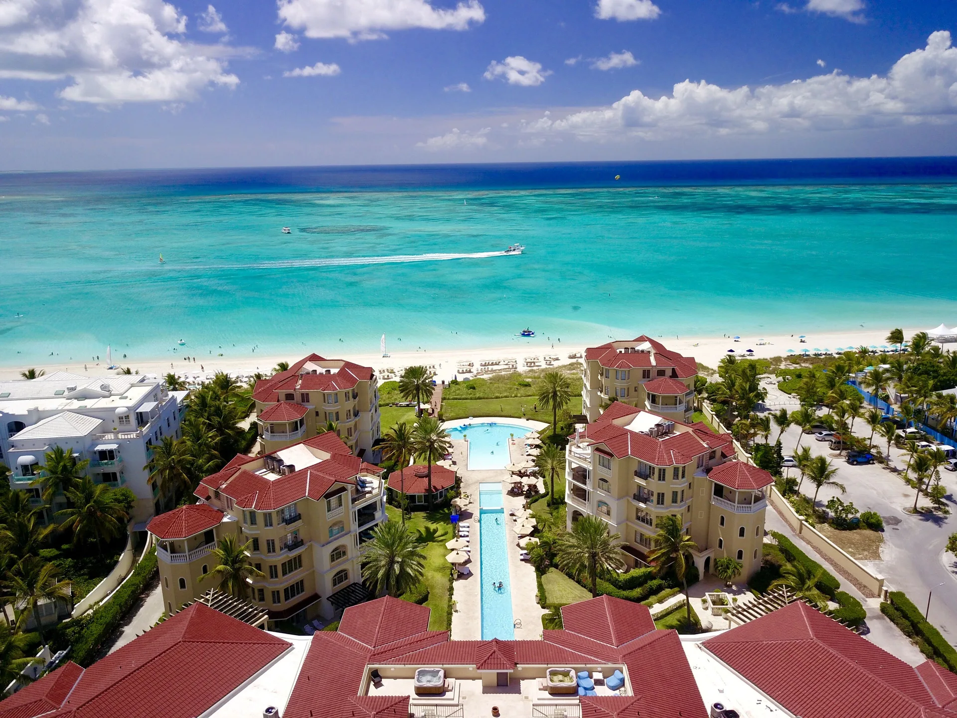 Aerial view of red-roofed resort buildings, pools, beach, and ocean at The Somerset on Grace Bay.