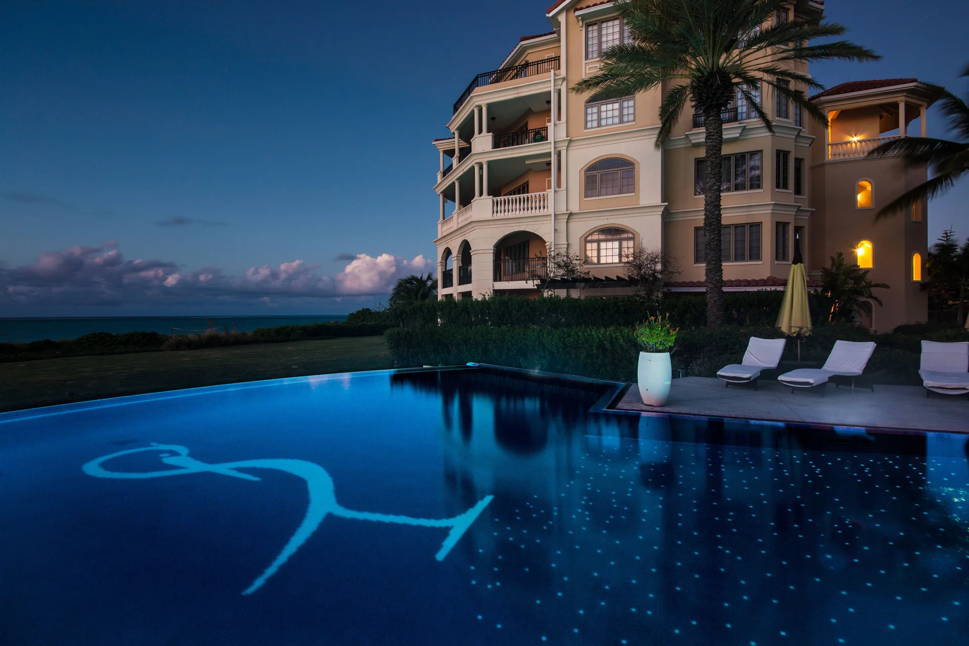 Evening pool with illuminated water, loungers, and ocean beside The Somerset on Grace Bay.