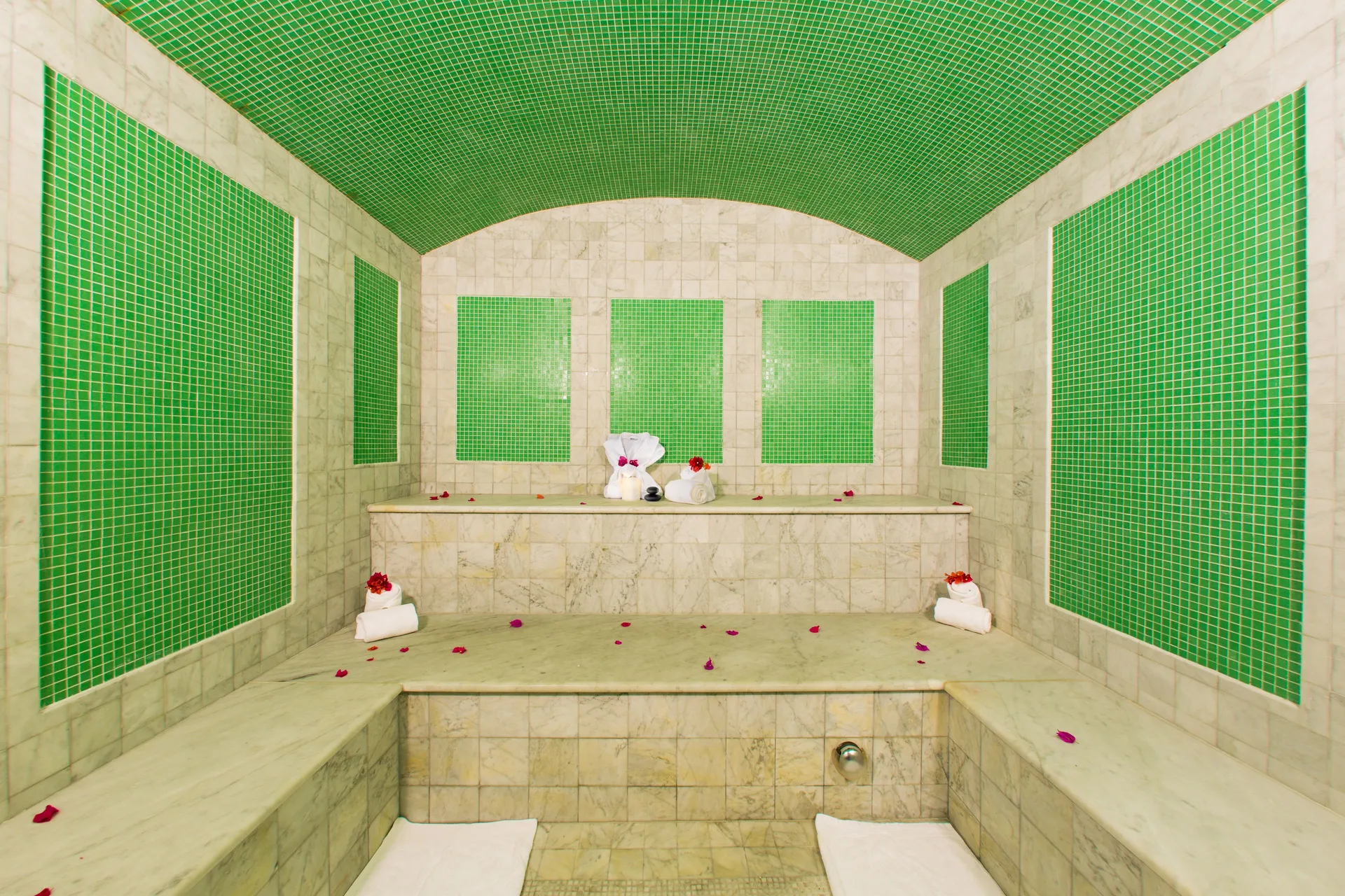 Steam room with green tile panels, marble benches, towels, and petals at The Somerset on Grace Bay.