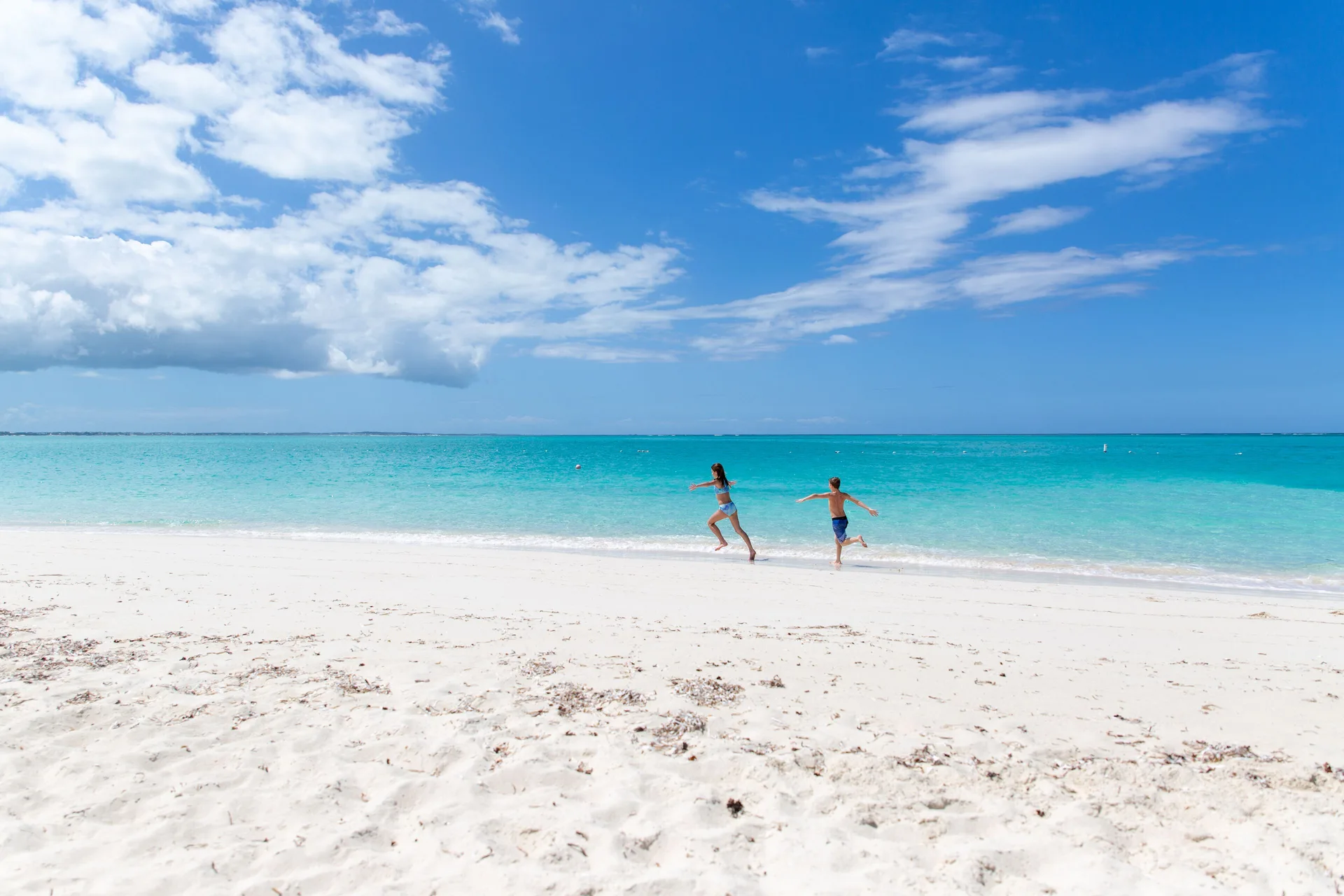 Children run along the white sand beach by turquoise water at The Somerset on Grace Bay.