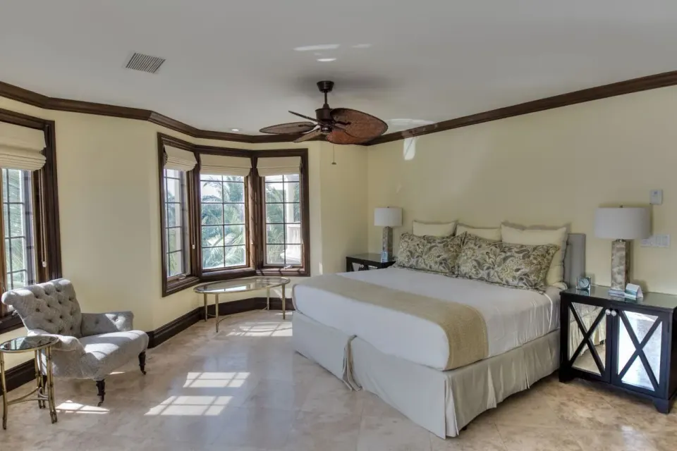 Guest bedroom with king bed, armchair, and sunlit bay windows at The Somerset on Grace Bay.