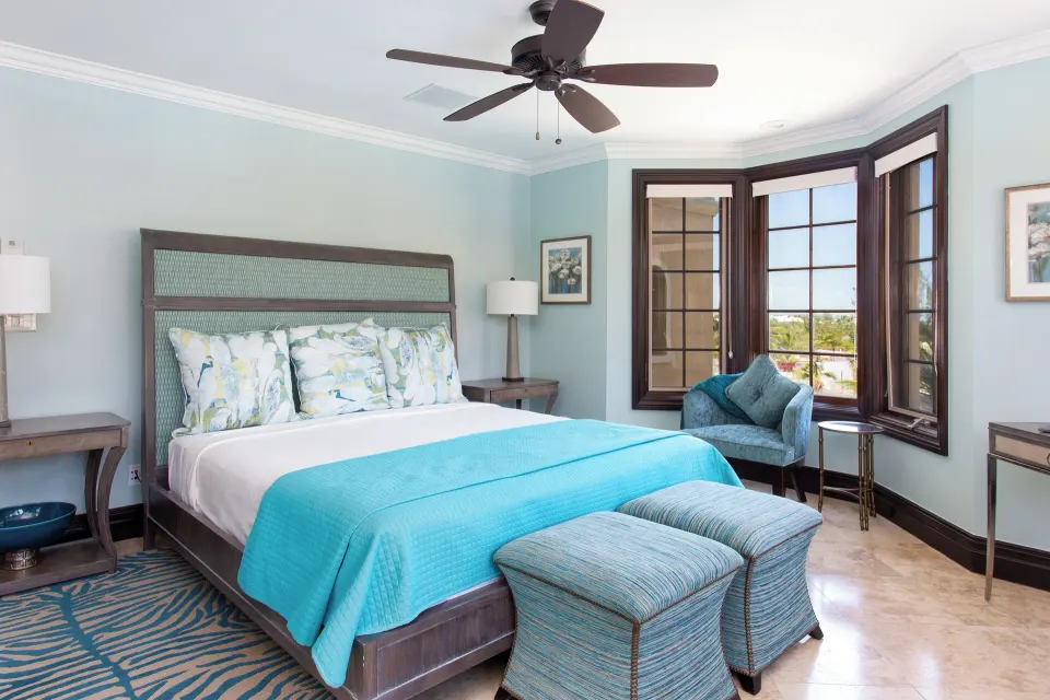 Guest bedroom with king bed, striped ottomans, and bay windows at The Somerset on Grace Bay.