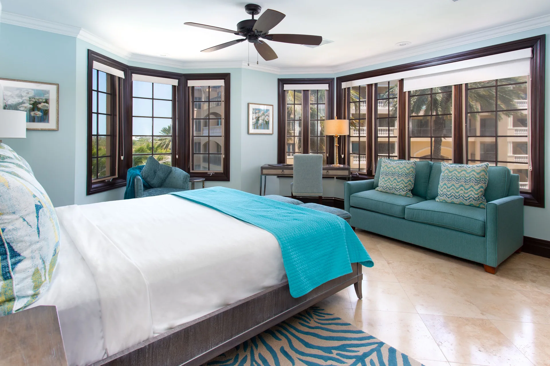 Guest bedroom with king bed, teal sofa, and bay windows at The Somerset on Grace Bay.