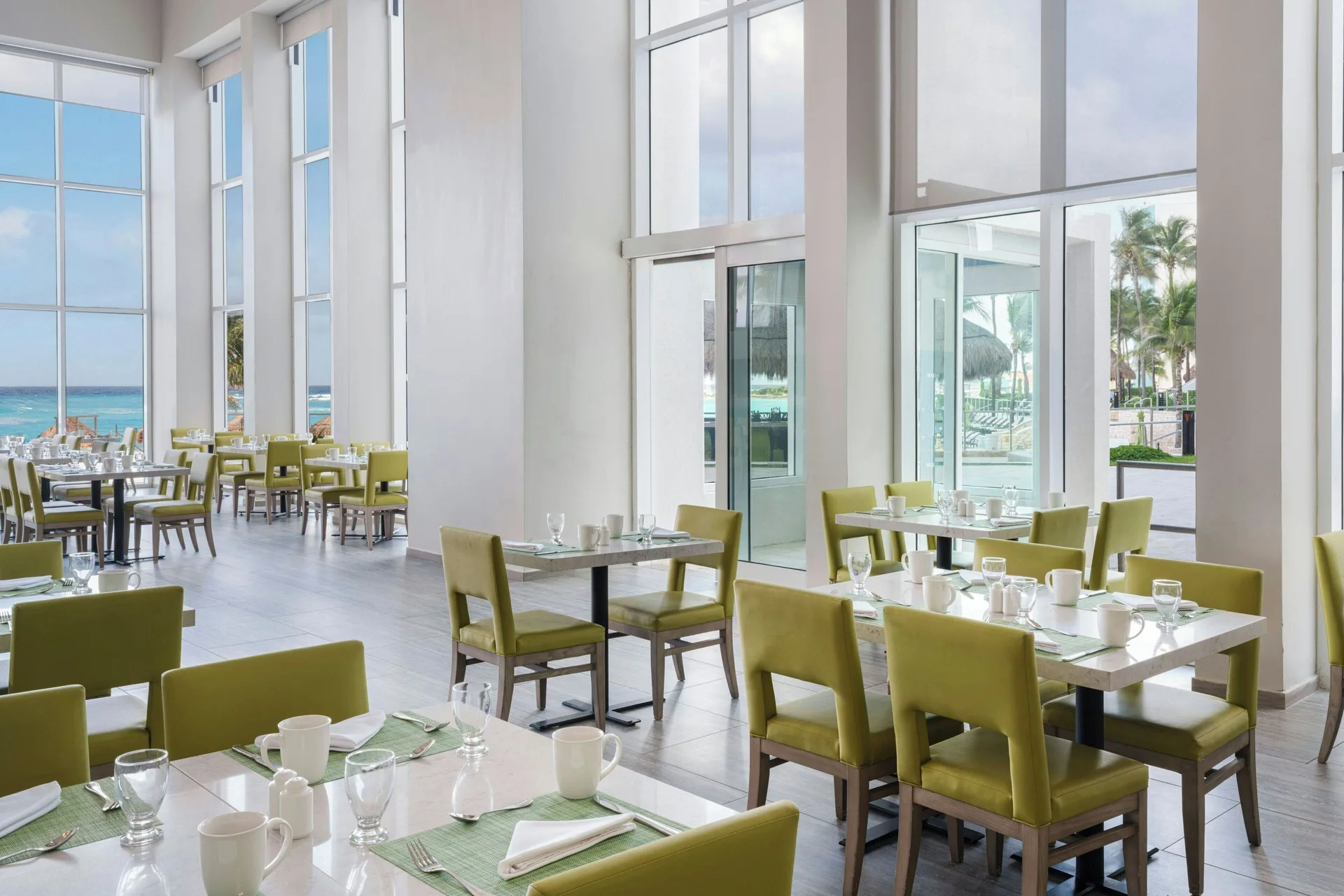 Bright dining room with green chairs and ocean-facing windows at The Westin Resort & Spa, Cancun.