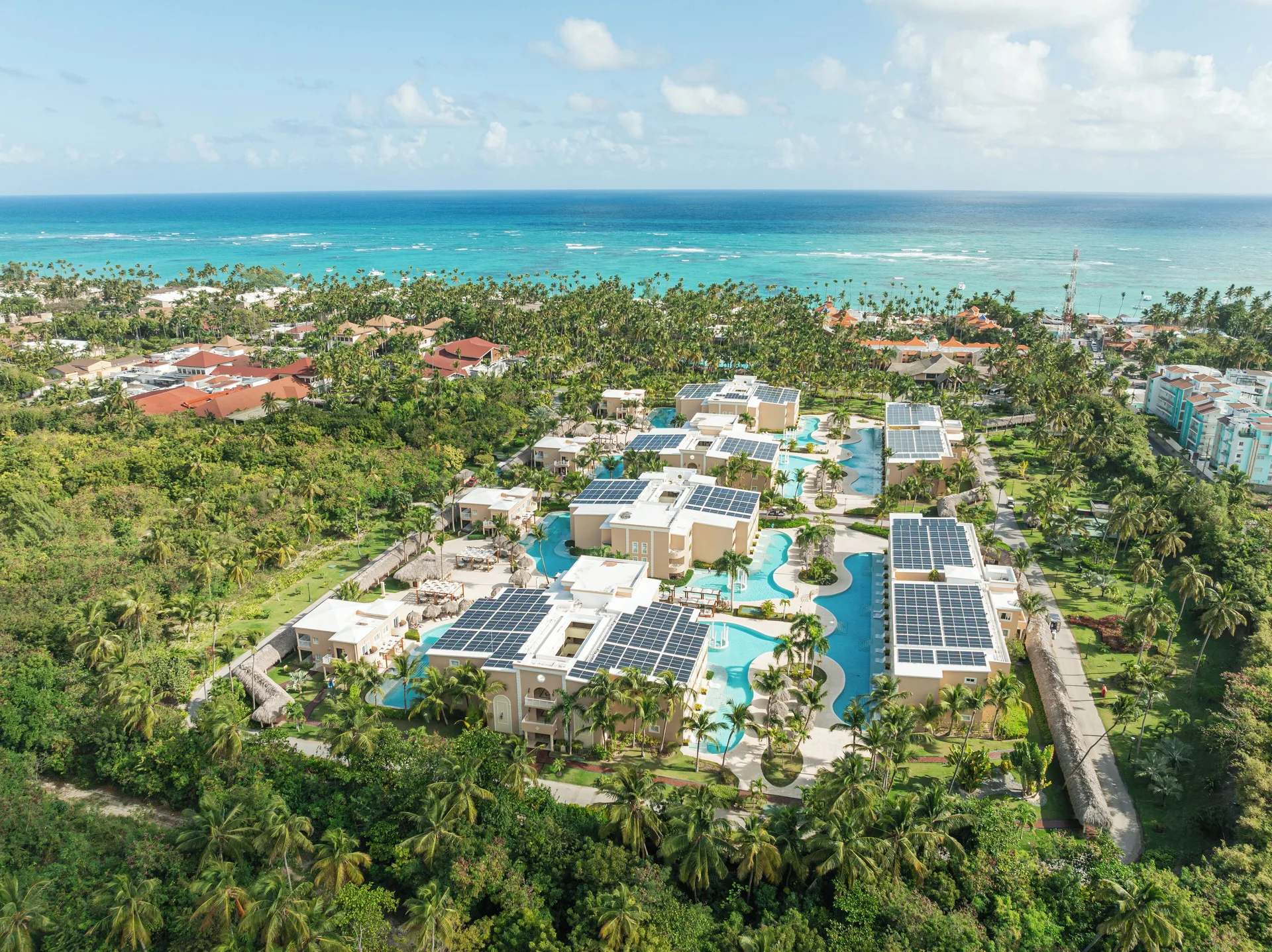 A wide aerial view shows TRS Turquesa Hotel between palms and the ocean.