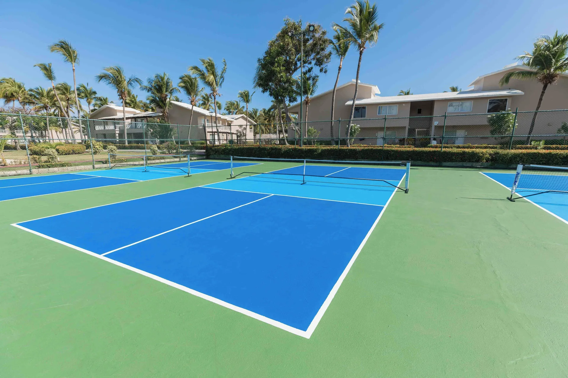 Blue and green pickleball courts beside palms and guest buildings at TRS Turquesa Hotel.