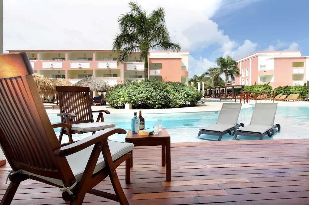 Pool deck with lounge chairs, drinks, and pink guest buildings at TRS Turquesa Hotel.