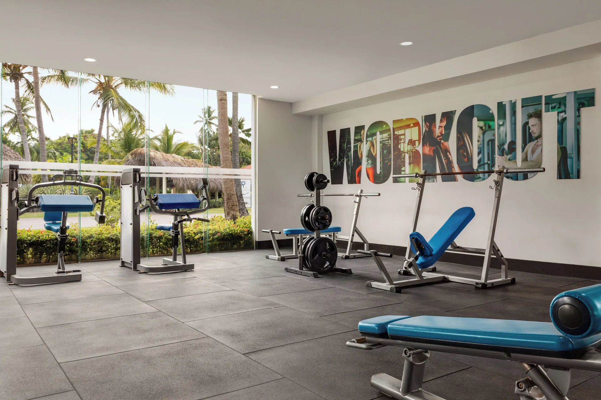 Weight room with blue benches and large windows at TRS Turquesa Hotel.