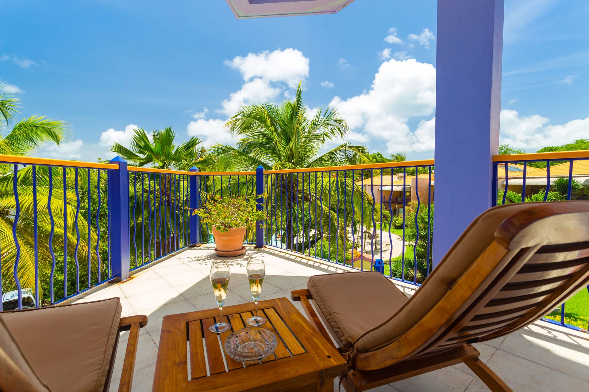 True Blue Bay Resort balcony at True Blue Bay Resort with loungers, drinks, palms, and blue railings.