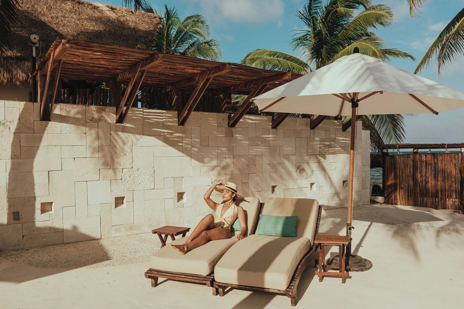 Guest reclining on a beach lounger under an umbrella at Viceroy Riviera Maya.