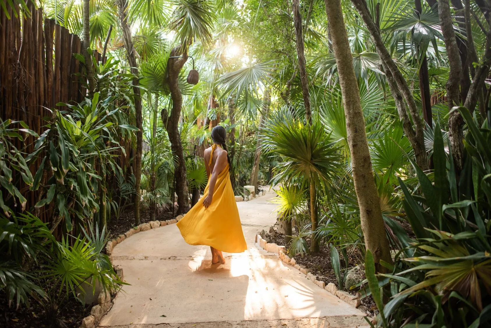 A guest in a yellow dress walks along a lush garden path at Viceroy Riviera Maya.