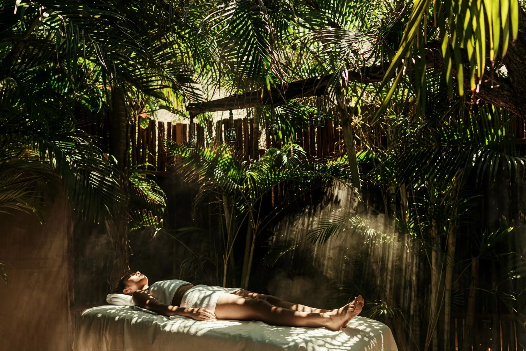 Guest resting on an outdoor spa bed beneath palms at Viceroy Riviera Maya.
