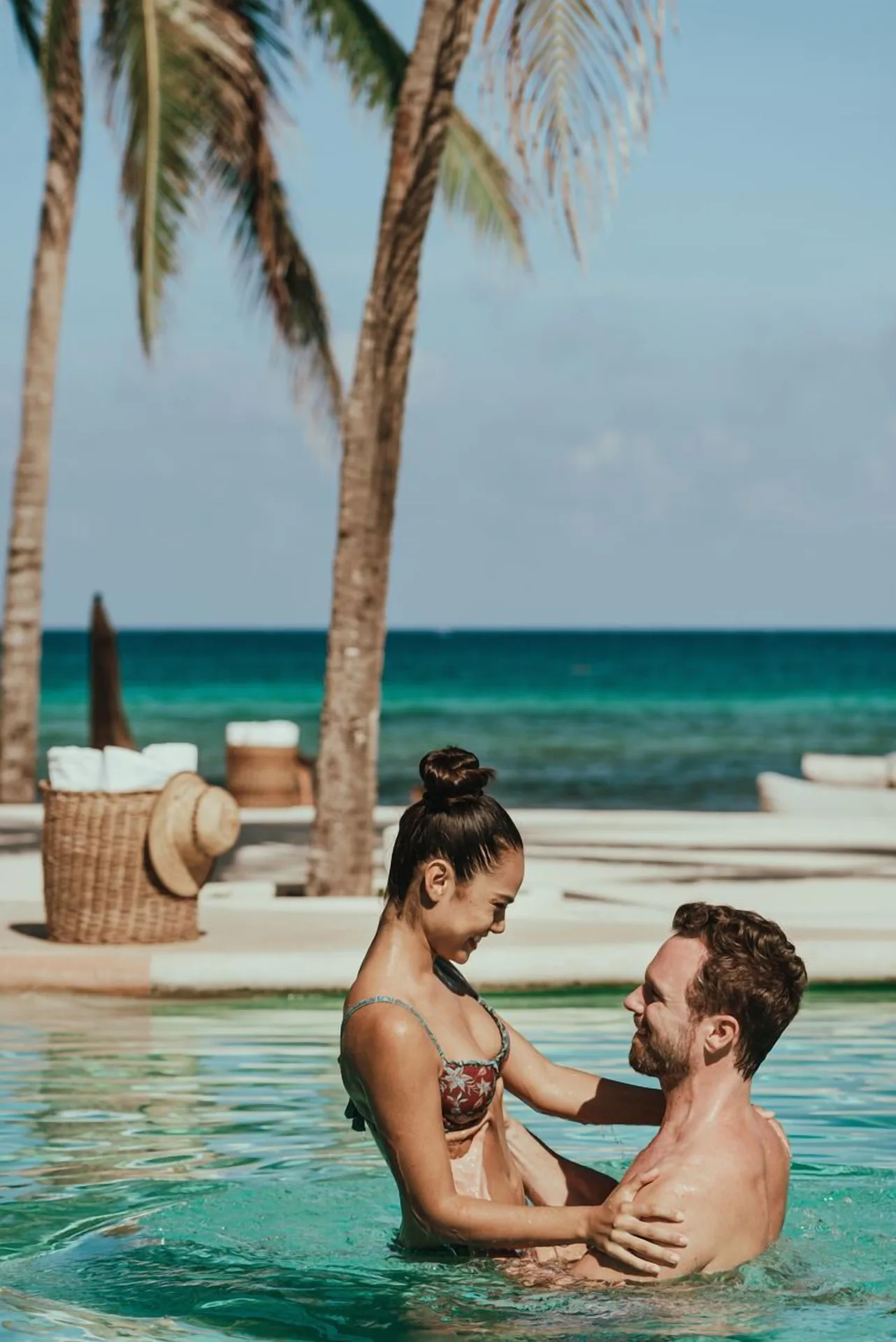Couple standing in the pool with palm trees and ocean at Viceroy Riviera Maya.