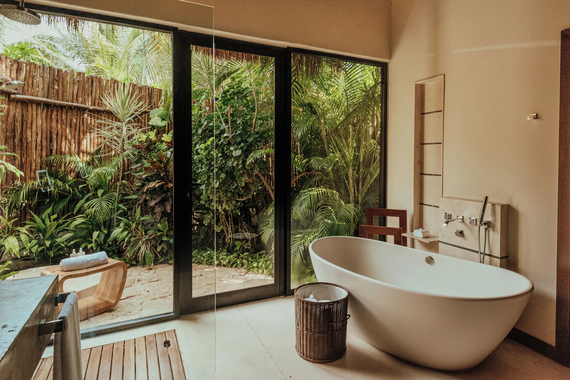 Villa bathroom with white tub, glass doors, and tropical plants at Viceroy Riviera Maya.