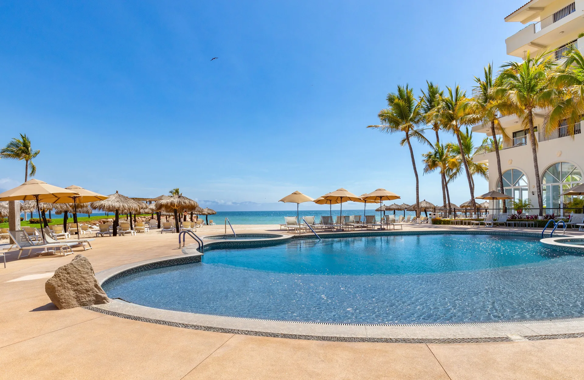Beachfront pool with umbrellas and ocean beyond at Villa del Palmar Beach Resort and Spa, Puerto Vallarta.