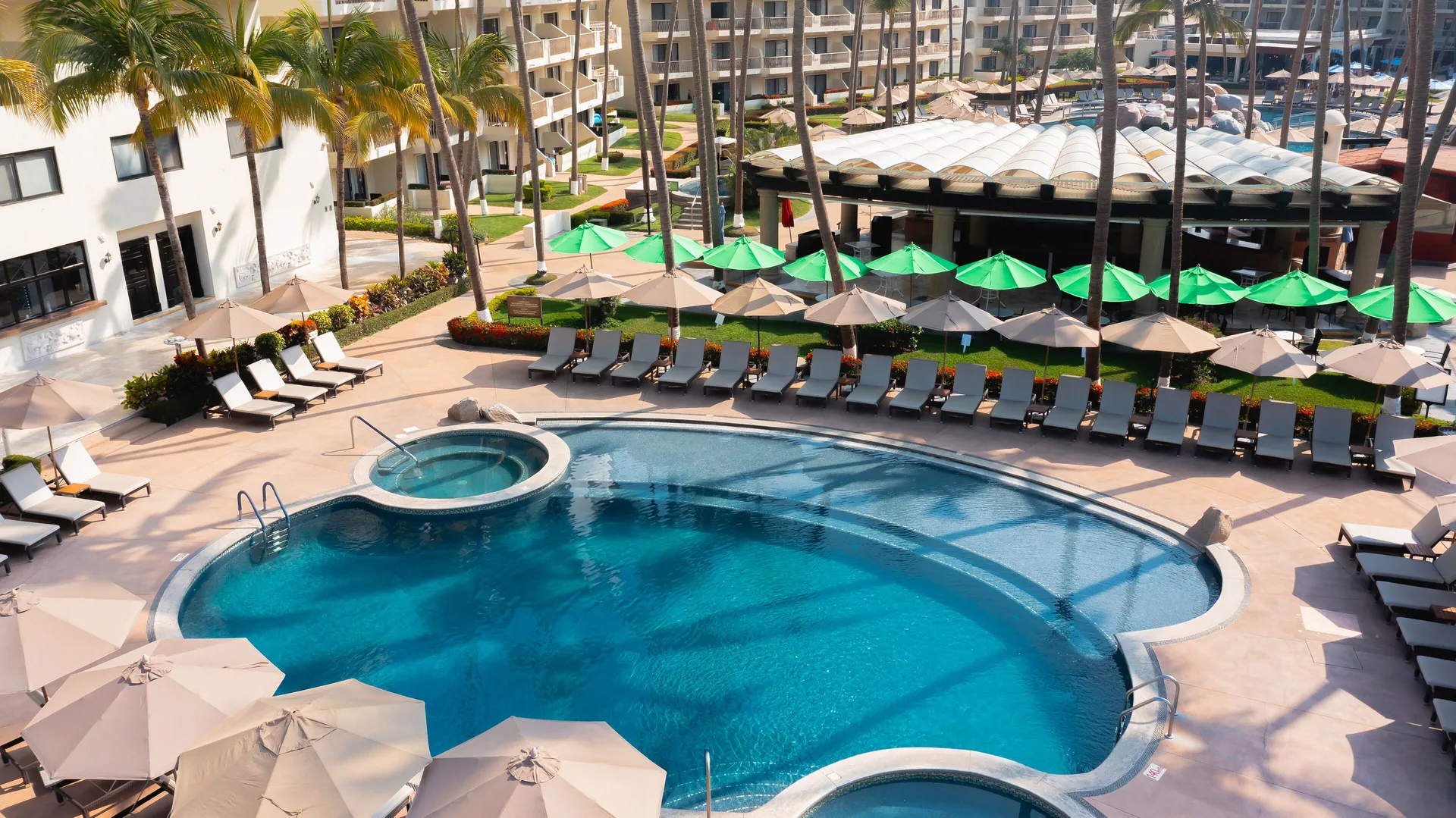 Curved pool with loungers and green umbrellas at Villa del Palmar Beach Resort and Spa, Puerto Vallarta.