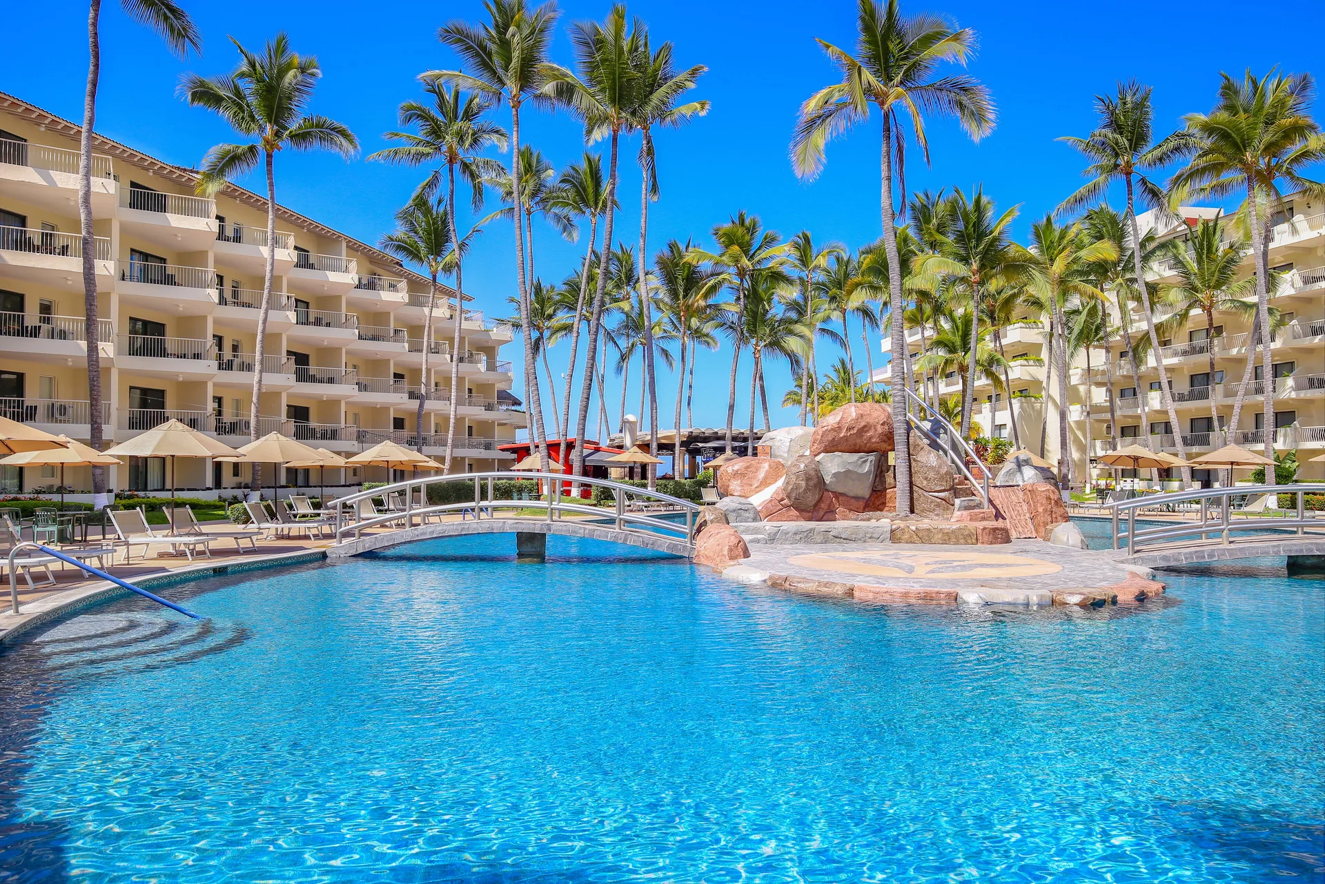 Palm-lined pool with bridge and rock feature at Villa del Palmar Beach Resort and Spa, Puerto Vallarta.