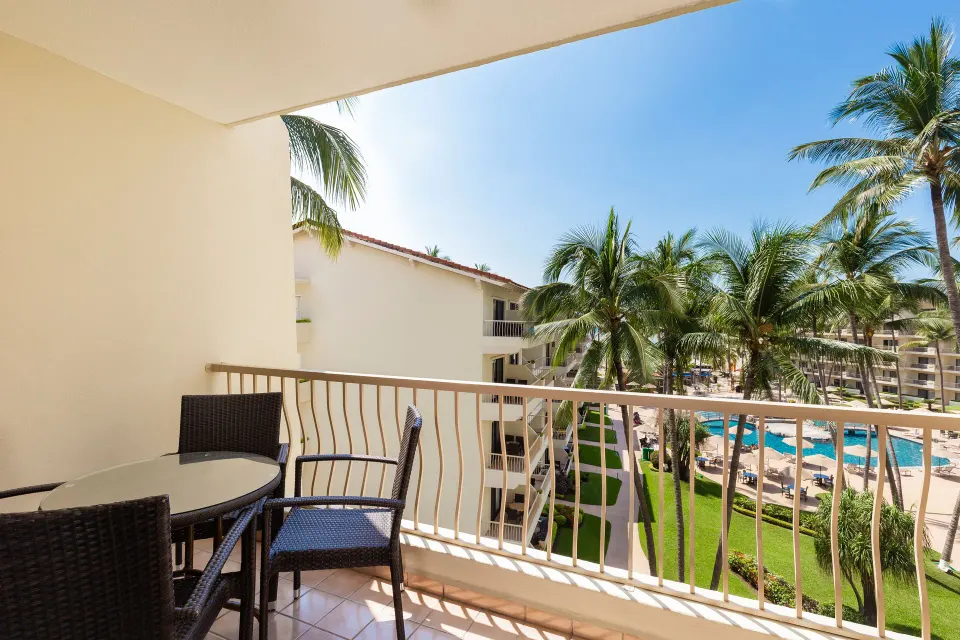 Junior Suite balcony with table, chairs, palms, and pool view at Villa del Palmar Beach Resort and Spa, Puerto Vallarta.