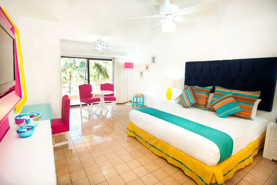 Junior Suite king bed with colorful pillows and balcony seating at Villa del Palmar Beach Resort and Spa, Puerto Vallarta.