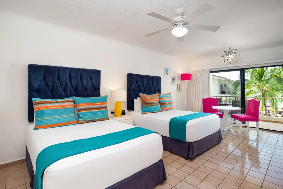 Junior Suite with two beds, balcony seating, and palm trees at Villa del Palmar Beach Resort and Spa, Puerto Vallarta.