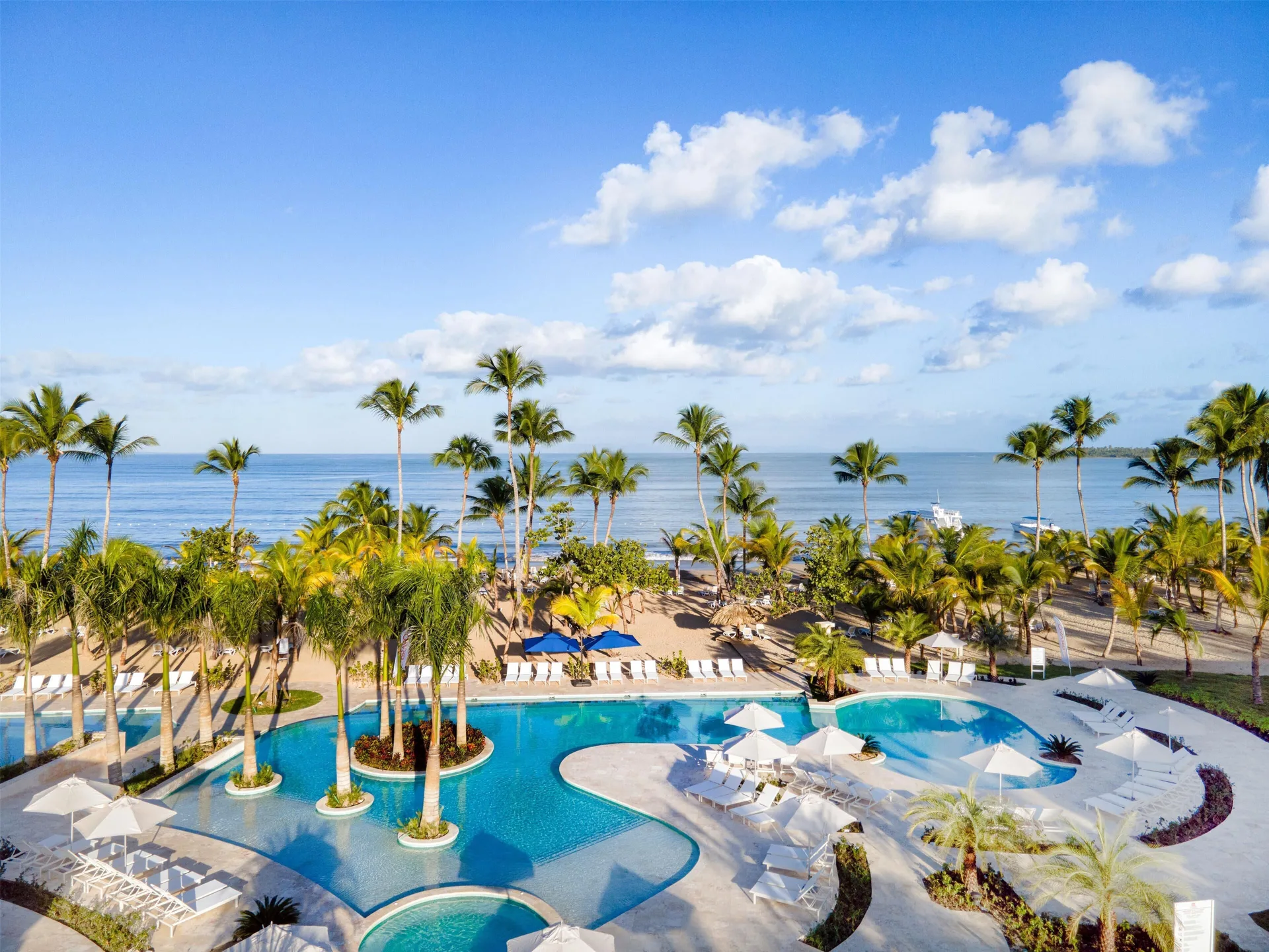 Palm-lined pool and oceanfront beach at Viva Miches under a blue sky.