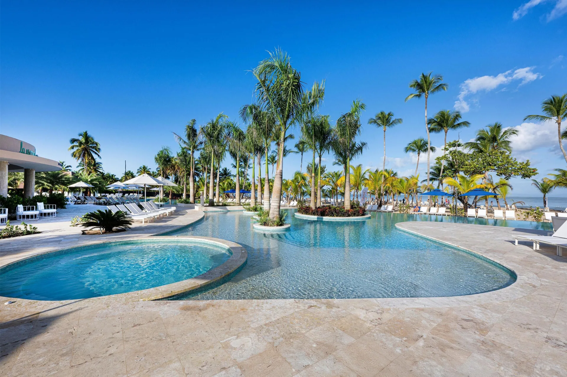 Curving pool with palm islands and loungers by the beach at Viva Miches.