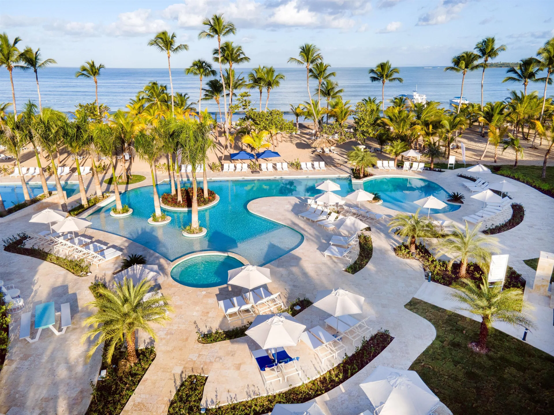 Pool deck with palm islands, white loungers, and the beach beyond at Viva Miches.