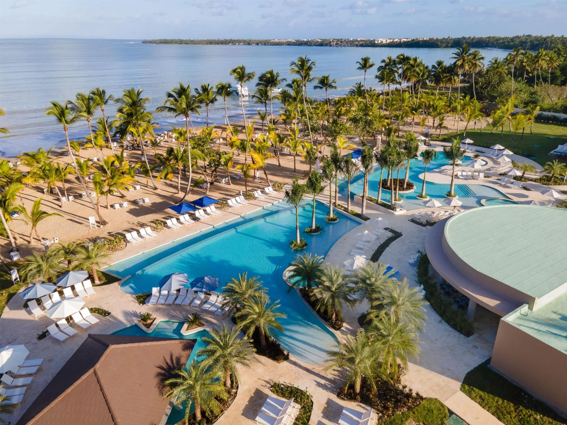 Aerial view of pools bordered by palms and a sandy beach at Viva Miches.
