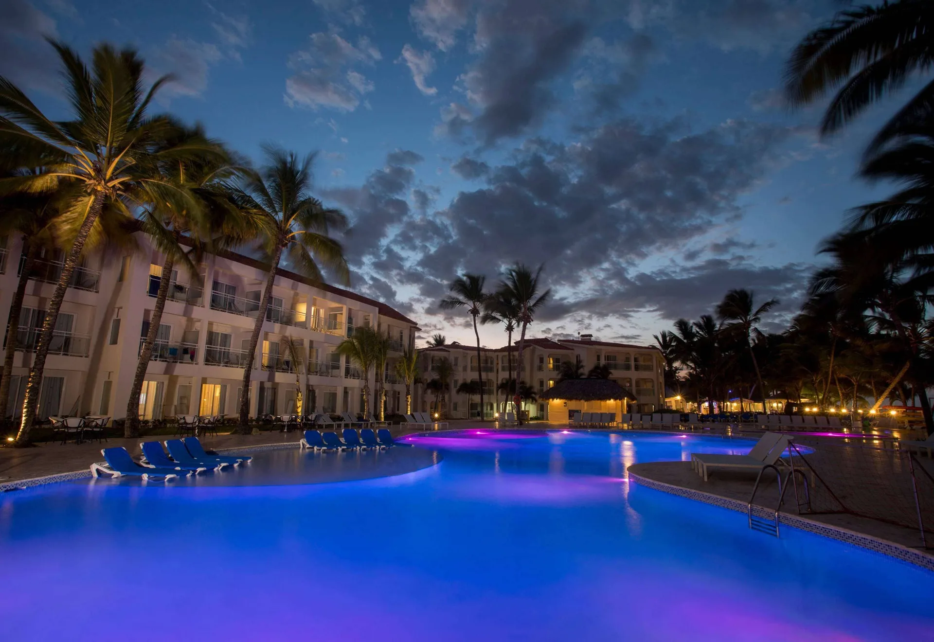 Illuminated pool at dusk with palms and resort buildings at Viva Tangerine.