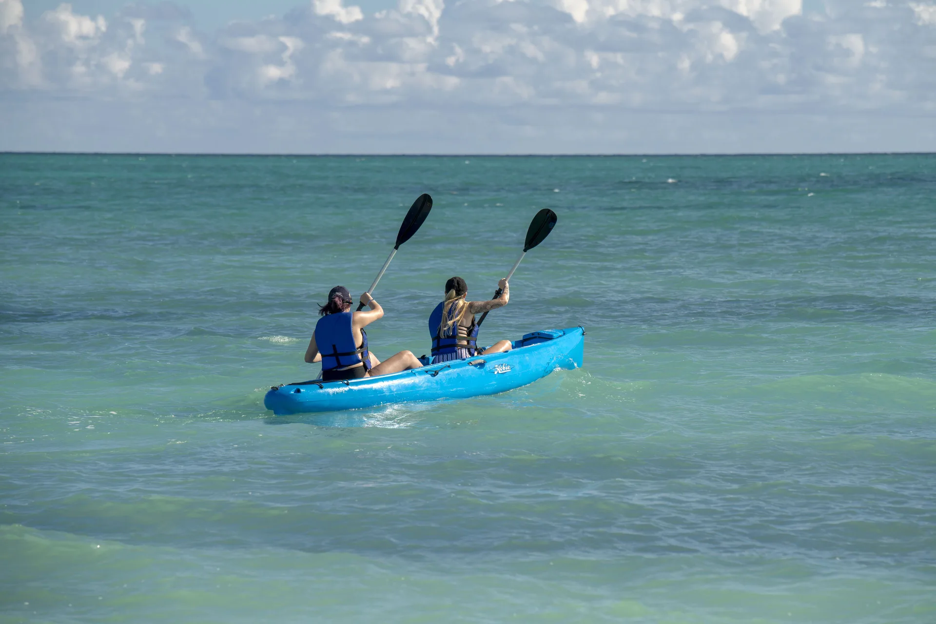 Two kayakers paddling a blue kayak on turquoise water at Viva Tangerine.