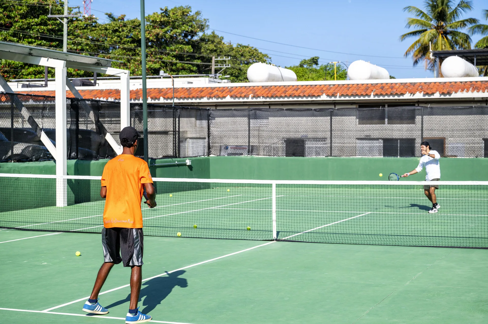 Two people practicing tennis on an outdoor green court at Viva Tangerine.