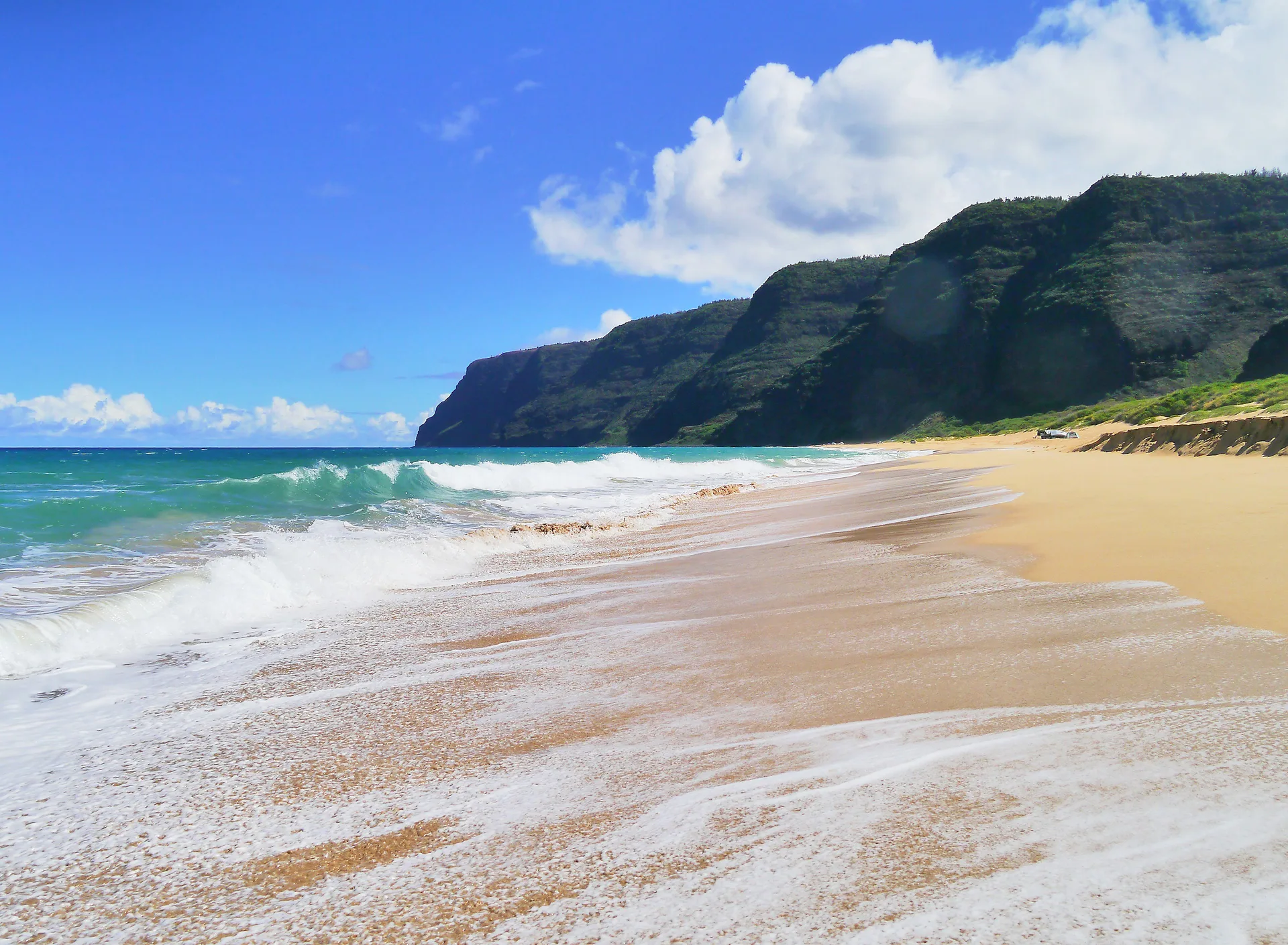 Sandy beach with waves and green cliffs near Waimea Plantation Cottages.