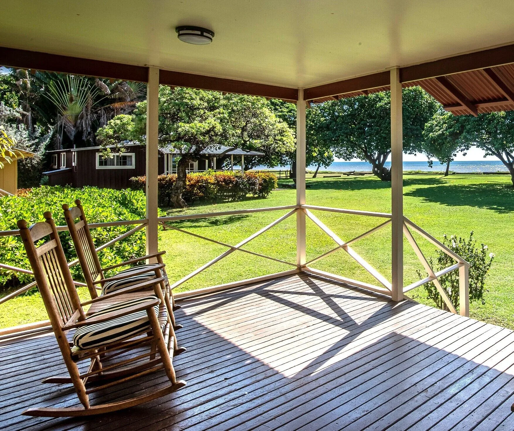 Coast Cottage porch with two rocking chairs and ocean beyond at Waimea Plantation Cottages.