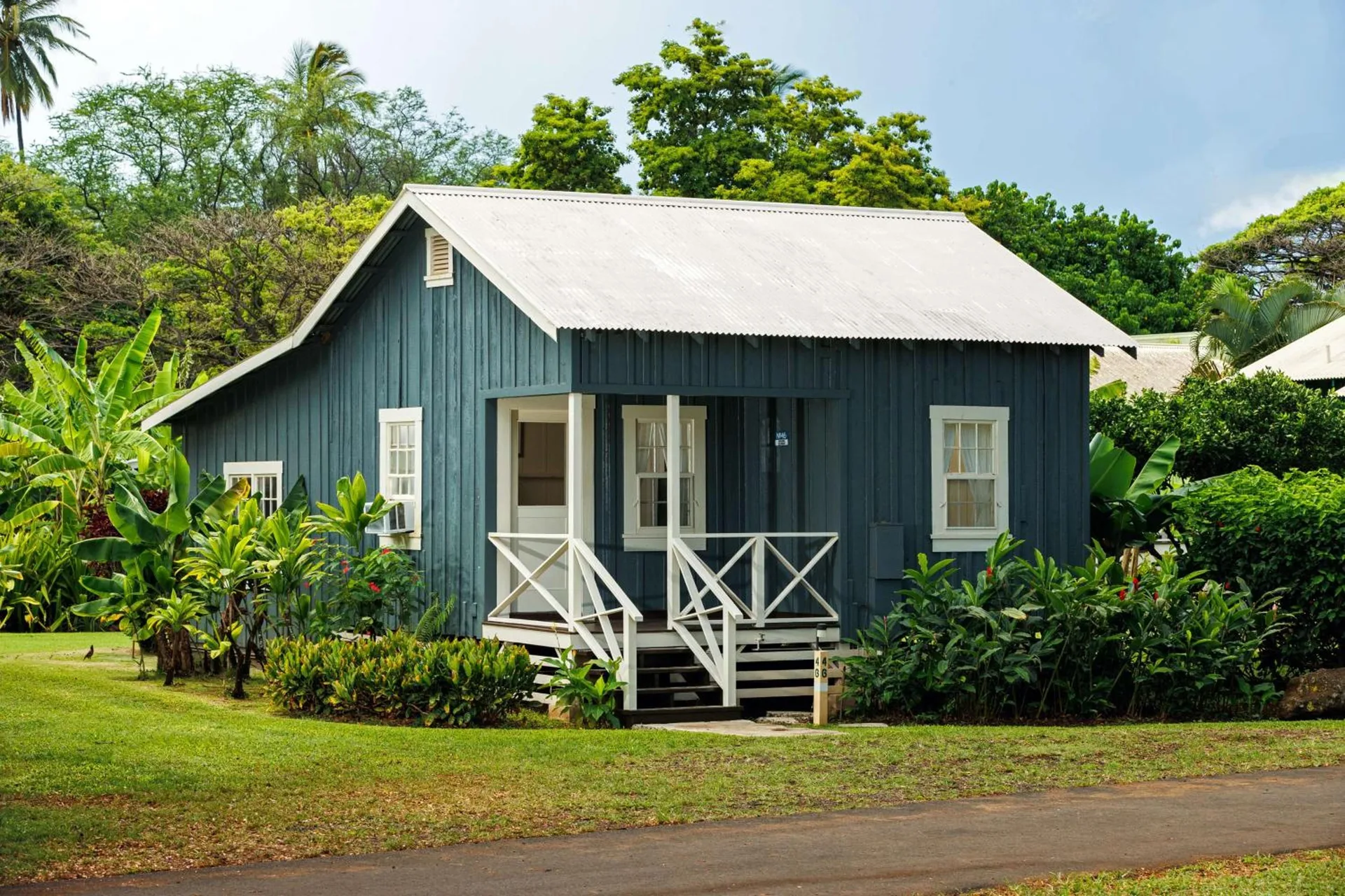 Blue garden-view cottage exterior with white porch railings and tropical landscaping at Waimea Plantation Cottages.